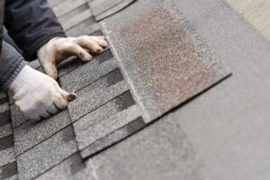 A close-up showing hands placing underlayment sheet on a wooden residential roof deck.