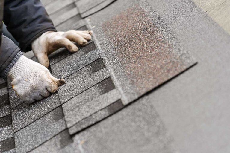 A close-up showing hands placing underlayment sheet on a wooden residential roof deck.