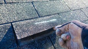 A construction worker installing a skylight on a shingled residential roof under partly cloudy skies.