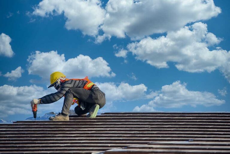 Homeowner examining shingles, flashing, and gutters on a snow-dusted residential roof.